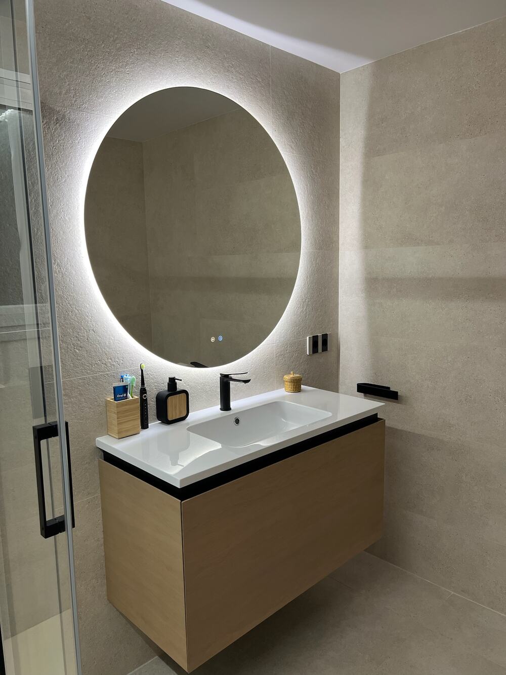 Baño con espejo redondo con luz LED y lavabo sobre mueble de madera