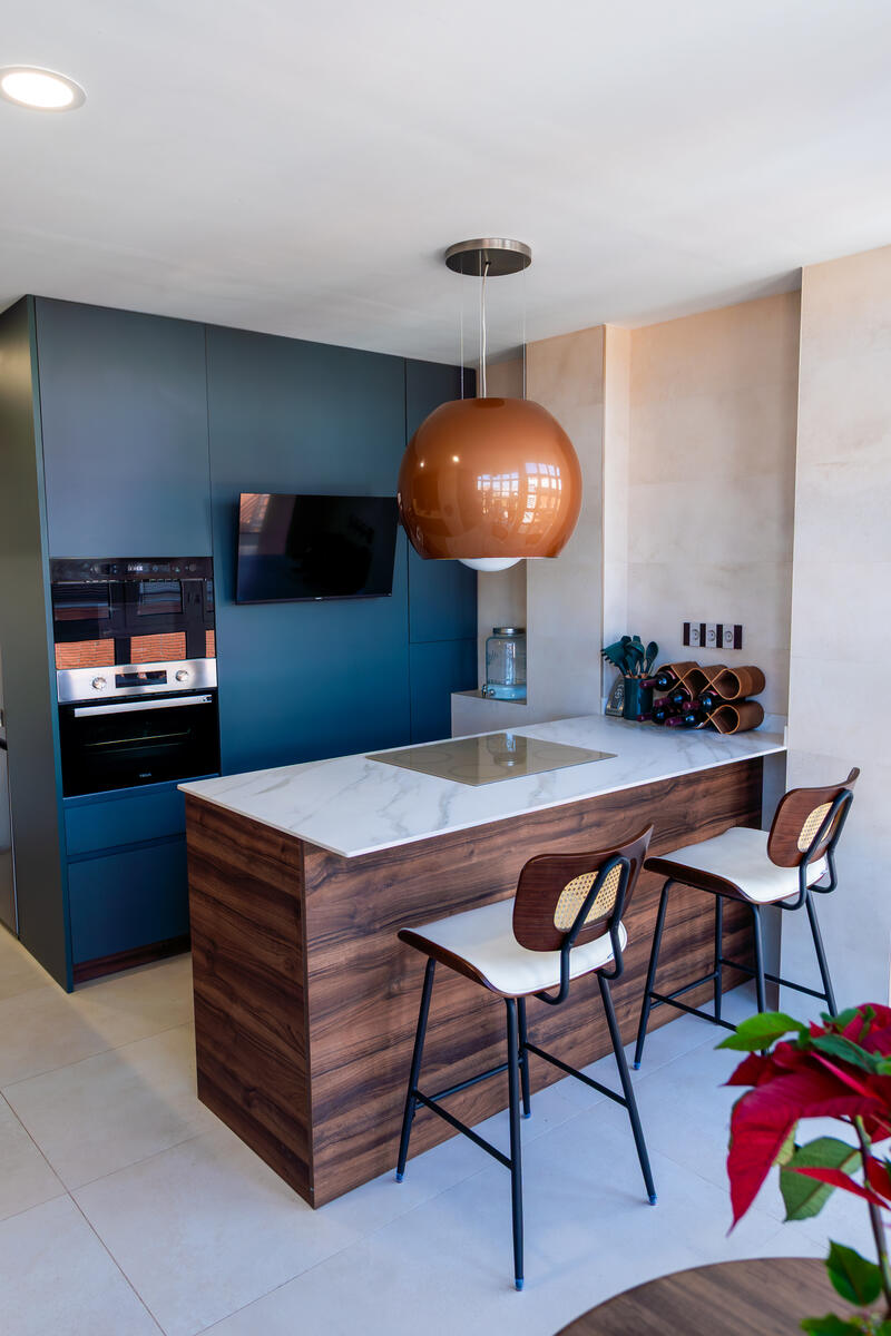 Cocina azul con isla de mármol y lámpara de cobre