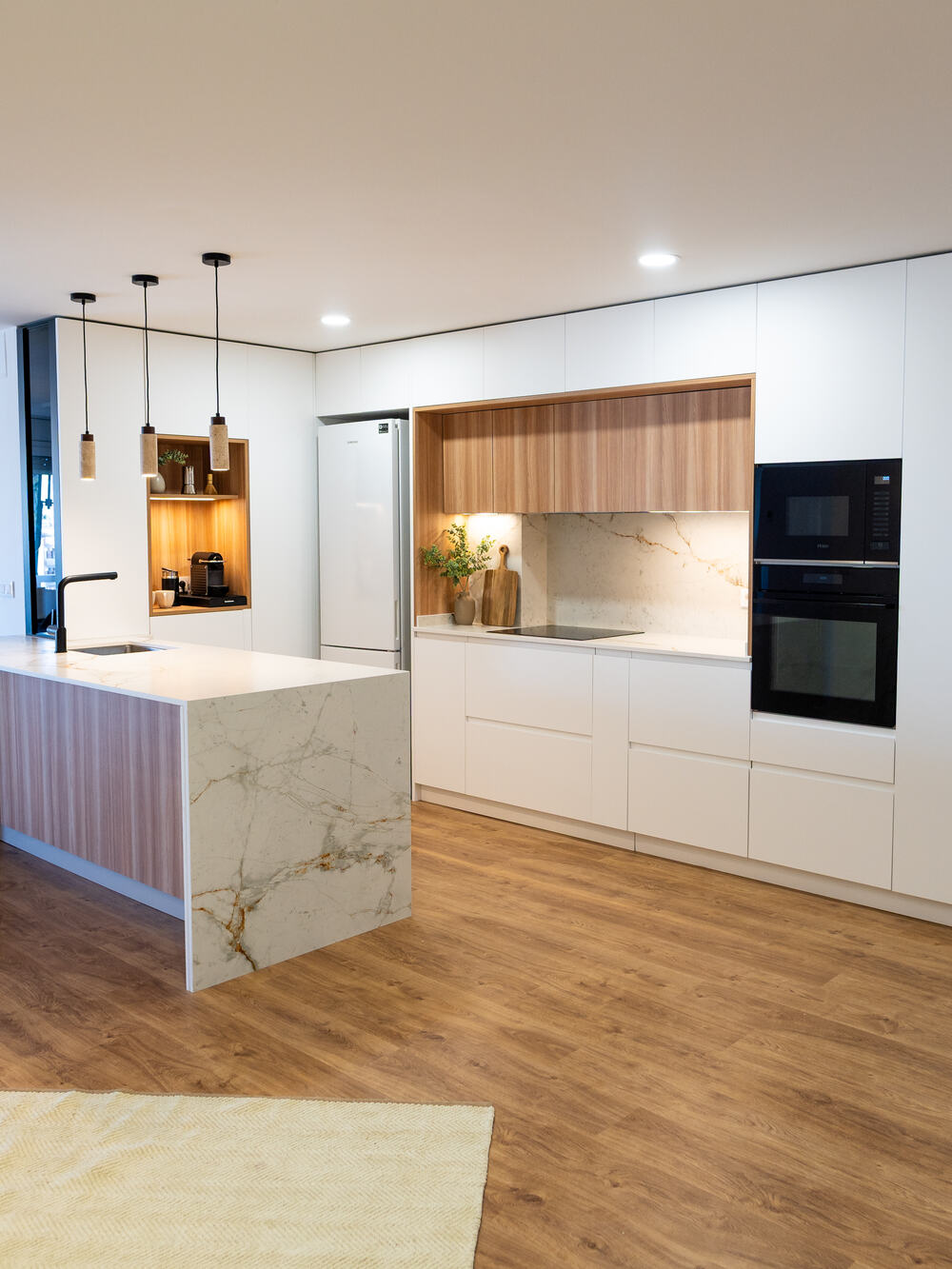 Cocina blanca con isla de mármol y nicho de madera