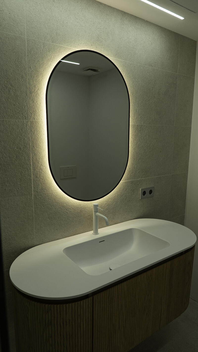 Baño con espejo ovalado con luz y lavabo blanco